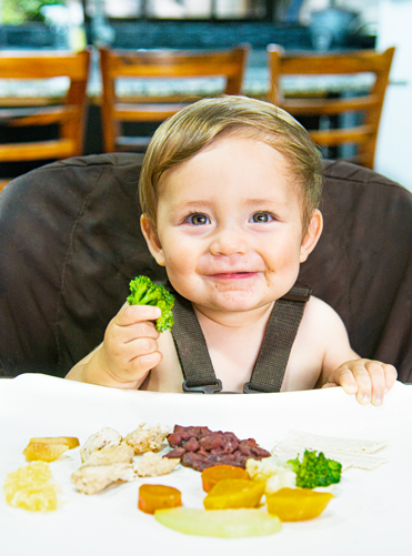 Niño en silla para bebes con frutas y verduras
