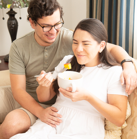 Mujer embarazada comiendo frutas abrazada por su pareja